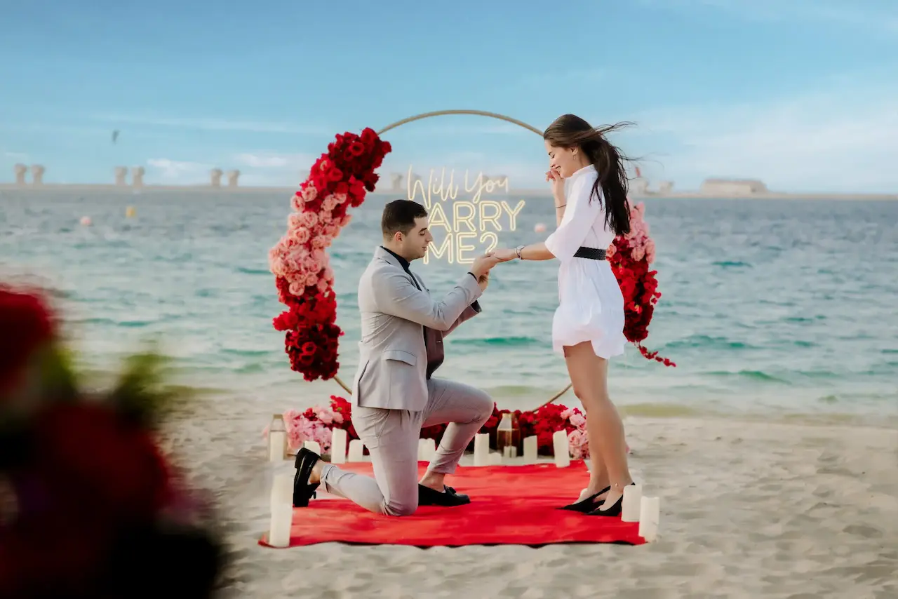 Beach wedding proposal in Dubai with floral arch and Will You Marry Me neon sign by the sea