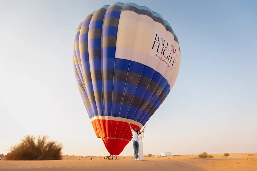 Couple posing beside a hot air balloon in the Dubai desert for a proposal experience