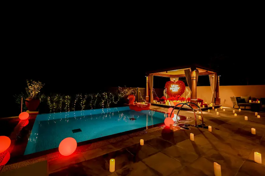Romantic poolside proposal setup at night in Dubai with glowing candles, red balloon lights, and Will You Marry Me gazebo display