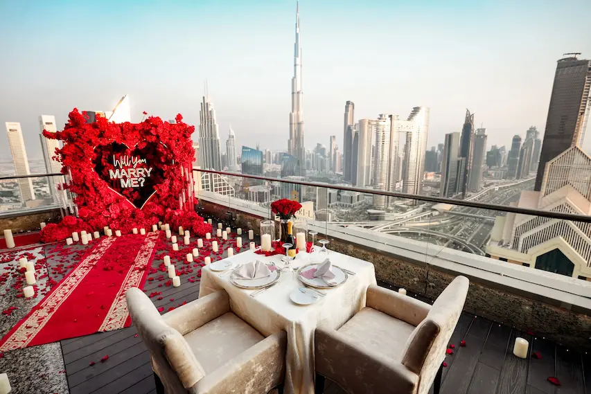 Rooftop proposal setup in Dubai with Burj Khalifa skyline view, red rose petals, candles, and Will You Marry Me heart display