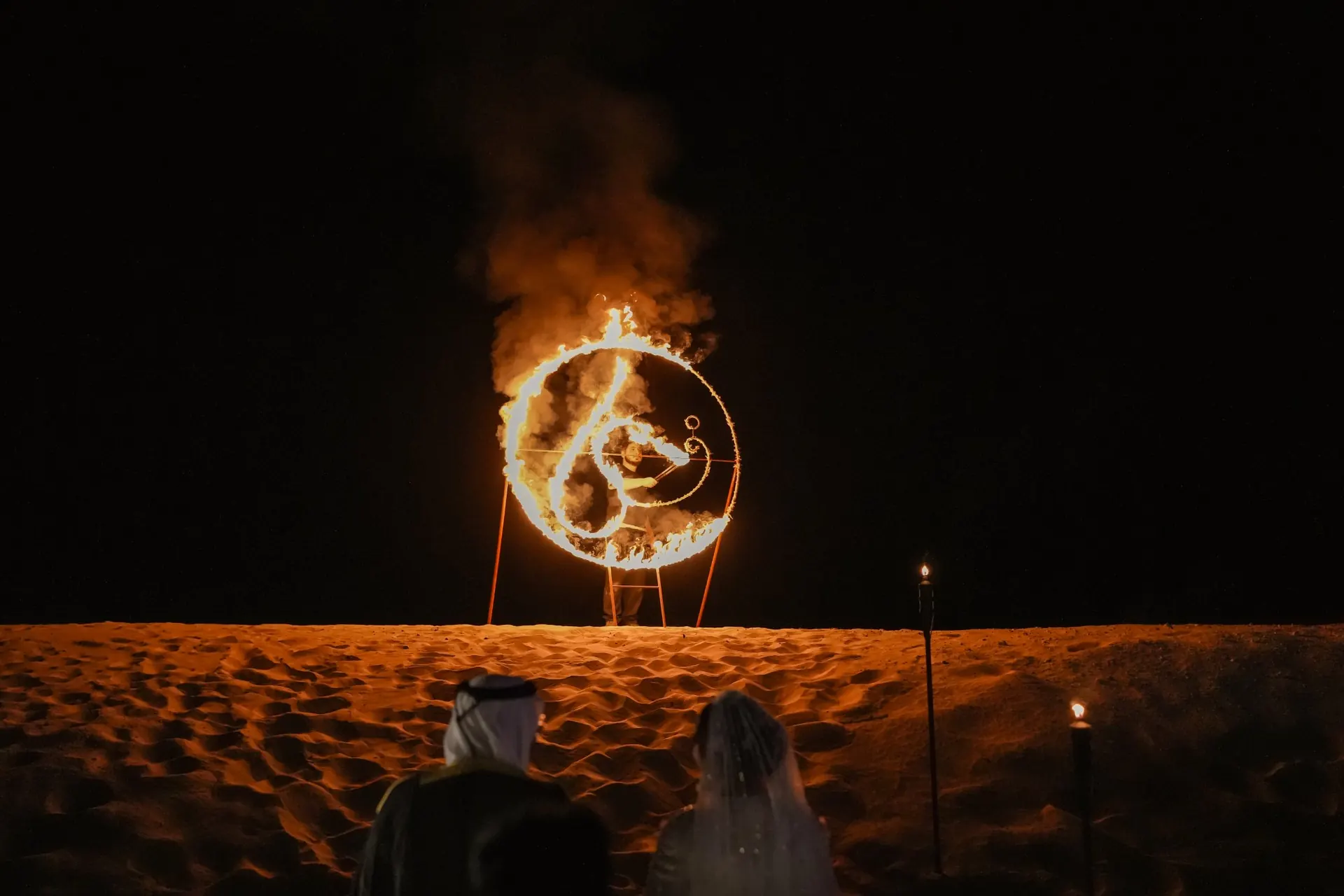 Guests watching a flaming monogram ring light up the dunes at a Dubai desert wedding
